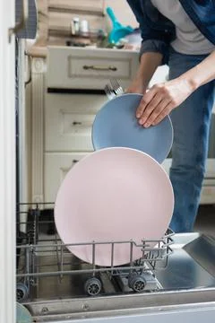 White woman washing dishes by hand or loading them into the dishwasher for Stock Photos