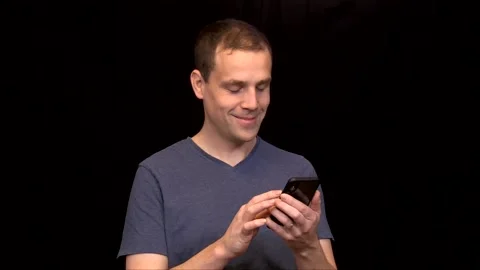 A white young Man on black background scrolling on his phone and typing close up Vidéo 146116664