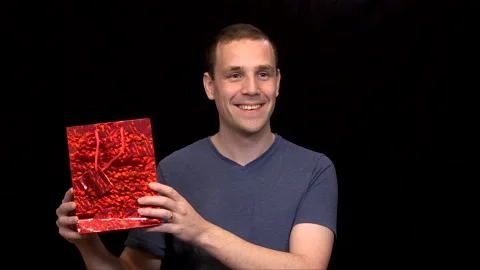 A white young Man on black background shows red present Vidéo 146263752