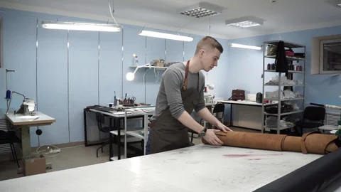White young tanner in an apron. On the table in the workshop he lays out the Stock Footage 104927262
