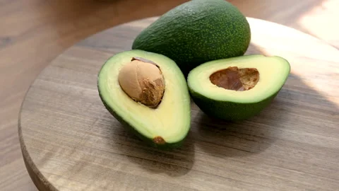 Whole and half avocado rotating on a wooden plate Stock Footage 272229005