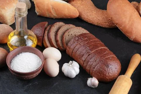 Whole and sliced bread, eggs, garlic, flour bowl and glass of oil Stock Photos