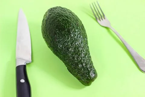 A whole avocado is on the table and a fork and knife are next to it. The conc Stock Photos