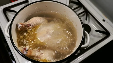 A whole chicken is cooking in a pot of boiling water in a home kitchen. Rich Stock Footage 329299059