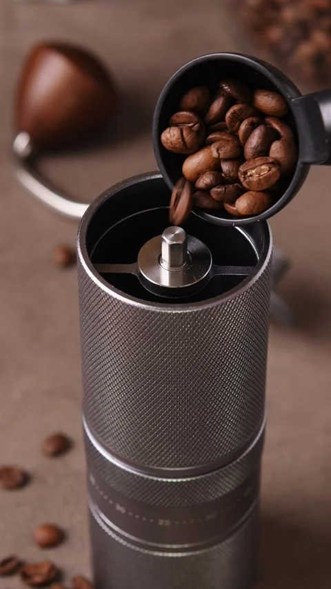 Whole coffee beans are poured from a black scoop into an open manual grinder in Stock Footage 346743249