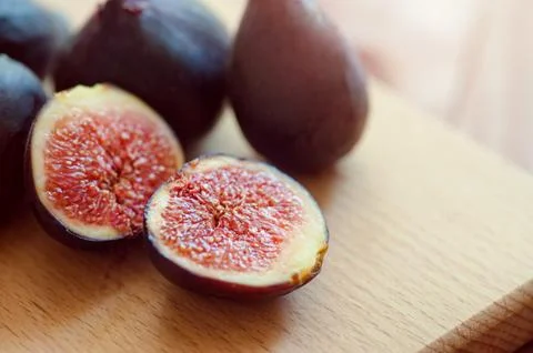 Whole figs and one fig sliced in half on top of a teak garden table. Focus is on Stock Photos