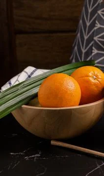 Whole fresh orange in wooden bowl on black stone table. Stock Photos