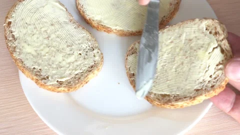 Whole-grain toast bread, buttered, on a white plate with a knife on the side Stock Footage 220292719