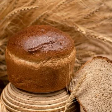 Whole loaf of crispy wheat bread. Slice of bread and wheat spikelets on blurred Stock Photos