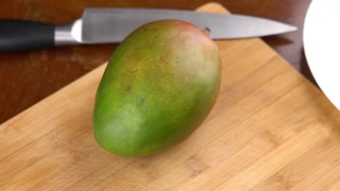 Whole mango fruit rotates back and forth on cutting board. Stock Footage 144670019