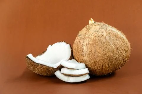 Whole mature coconut and multiple sliced halves on brown background Stock Photos