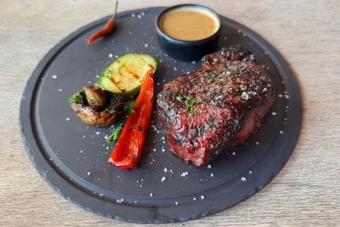 Whole Medium Rare beef steak with grilled vegetables on dish Stock Photos