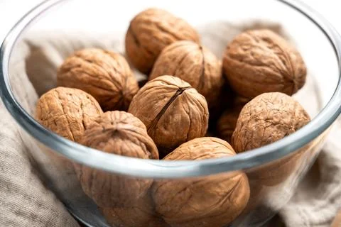 Whole raw walnuts with nutshells in glass bowl. Close-up. Stock Photos