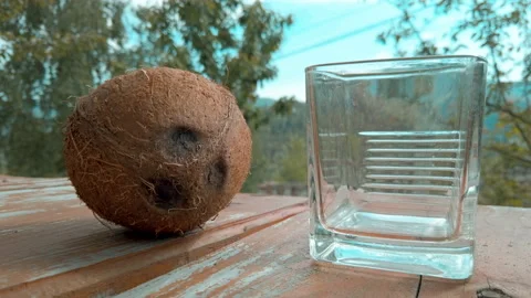 Whole ripe coconut on table next to transparent glass. Male hand taking coconut Видео 132729188
