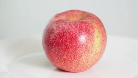 Whole ripe pink apple fruit on white plate rotates Stock Footage 102448879