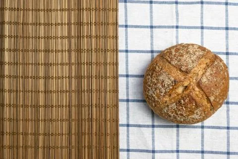 Whole rye bread placed and brown bamboo mat over table cloth with grid patter. Stock Photos