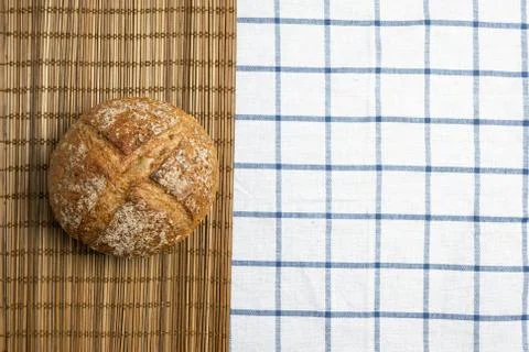 Whole rye bread placed on brown bamboo mat over table cloth with grid pattern Stock Photos