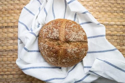 Whole rye bread placed on white cloth with blue stripe over wicker texture. Stock Photos