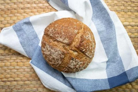 Whole rye bread placed on white cloth with blue stripe over wicker texture. Stock Photos