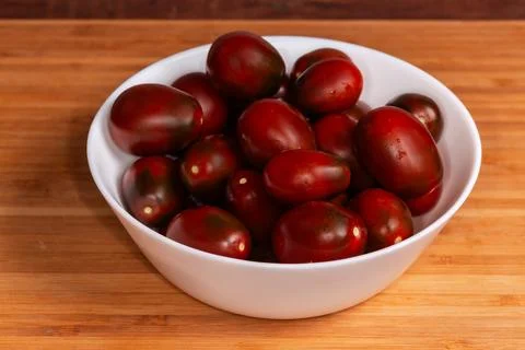 Whole small reddish brown plum tomatoes in white bowl Stock Photos