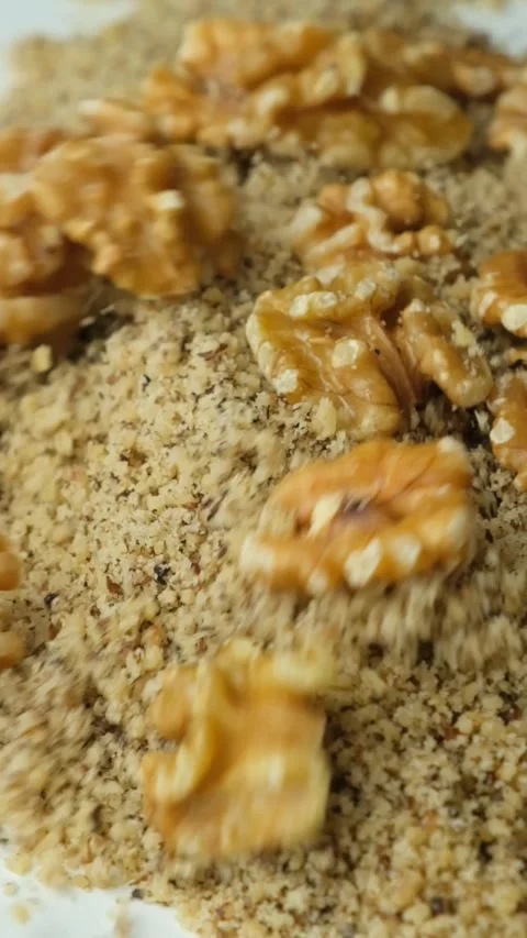 Whole walnut halves poured on crushed walnut kernels flour slow motion vertical Stock Footage 326348680