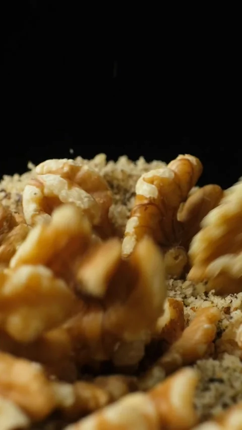 Whole walnut halves poured on crushed walnut kernels flour slow motion vertical Stock Footage 326348876
