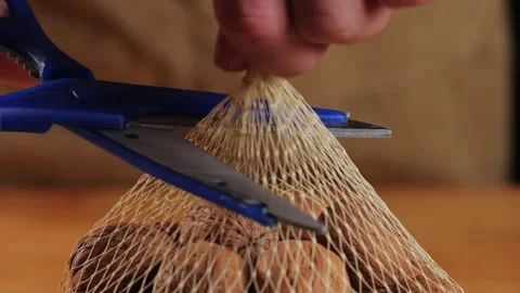 Whole walnut in a mesh bag close-up. Man open with a scissors a bag with nuts Stock Footage 256678295