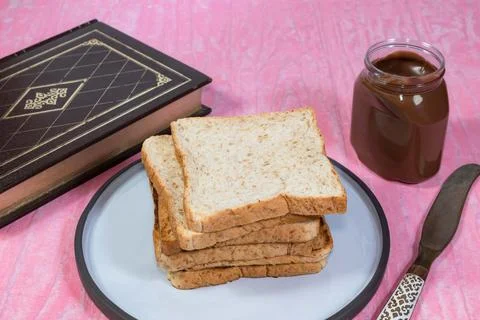 Whole wheat bread loaf slice has chocolate book on pink table. Stock Photos