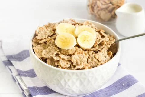 Whole wheat breakfast cornflakes with banana served in a white bowl Stock Photos