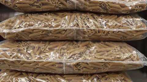 Whole wheat penne pasta packed in clear bags and stacked for retail sale Stock Footage 345978908
