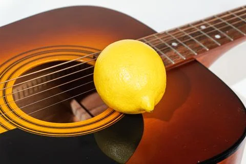 Whole yellow lemon resting on the strings of an acoustic guitar Stock Photos