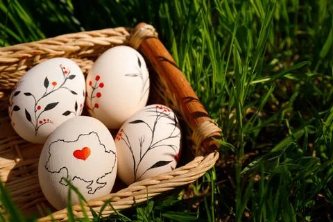 Wicker basket with decorated Easter eggs in green grass outdoors, closeup. Sp Stock Photos