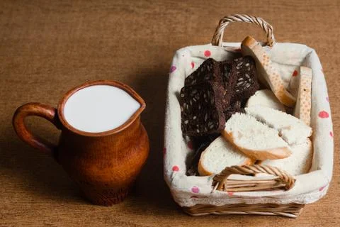 Wicker basket with different sliced bread and a jug of milk on the table. Hom Stock Photos