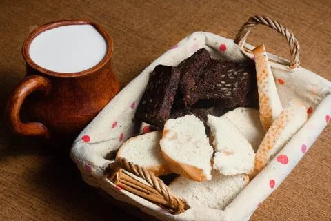 Wicker basket with different sliced bread and a jug of milk on the table. Hom Stock Photos