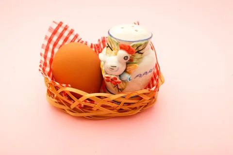 Wicker basket with Easter eggs and salt cellar in the form of a chicken on pink Stock Photos