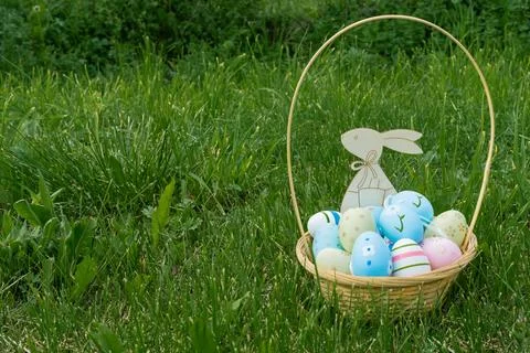 A wicker basket with Easter eggs and a wooden hare on the green grass, lawn Fotos Stock