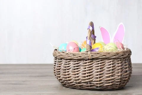 Wicker basket with Easter eggs and funny bunny ears on wooden table against l Stock Photos
