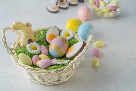 Wicker basket with easter sweets and colorful eggs on white marble stone tabl Stock Photos