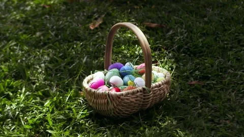 Wicker basket filled with colorful Easter eggs placed on green grass in garden Vídeos de archivo 330376040