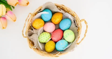 A wicker basket filled with colorful Easter eggs on a white table with tulips Stock Footage 331505416
