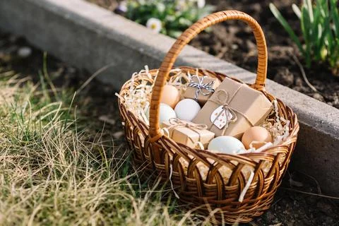 Wicker basket filled with Easter eggs and small gift boxes on a grassy ground Stock Photos