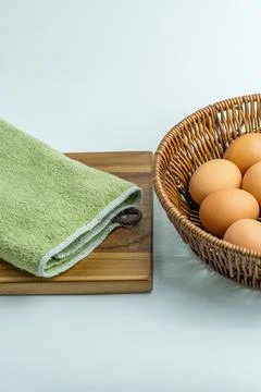 Wicker basket full of brown eggs next to folded kitchen towel isolated on whi Stock Photos