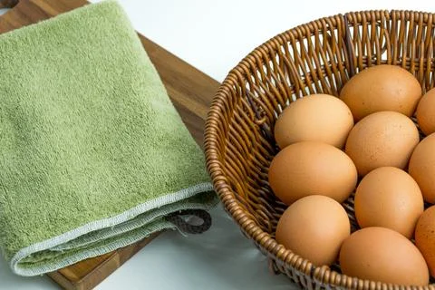 Wicker basket full of brown eggs next to folded kitchen towel isolated on whi 库存照片