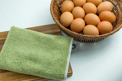 Wicker basket full of brown eggs next to folded kitchen towel isolated on whi 库存照片