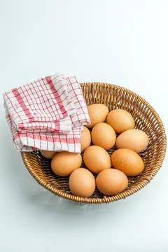 Wicker basket full of brown eggs next to folded kitchen towel isolated on whi Stock Photos