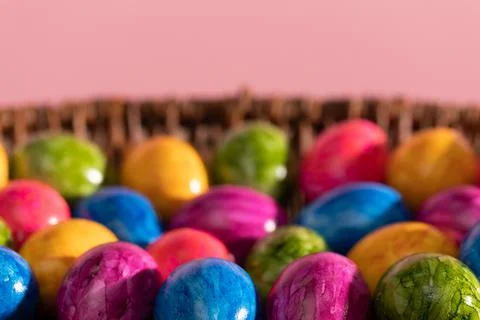 Wicker basket full of colorful Easter eggs on pink solid background. Easter. 写真素材