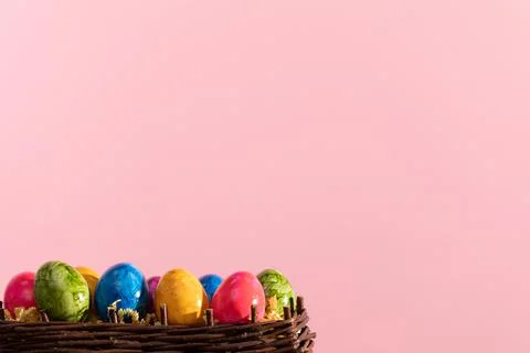 Wicker basket full of colorful Easter eggs on pink solid background. Easter. 写真素材