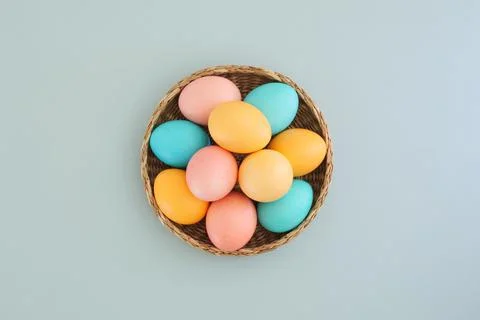 Wicker basket full of easter colorful eggs on blue background, top view, flat Stock Photos