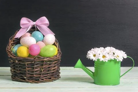 Wicker basket full of painted Easter eggs and a pink ribbon bow and a green 库存照片