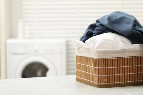 Wicker basket with laundry on light table in bathroom. Space for text Stock Photos